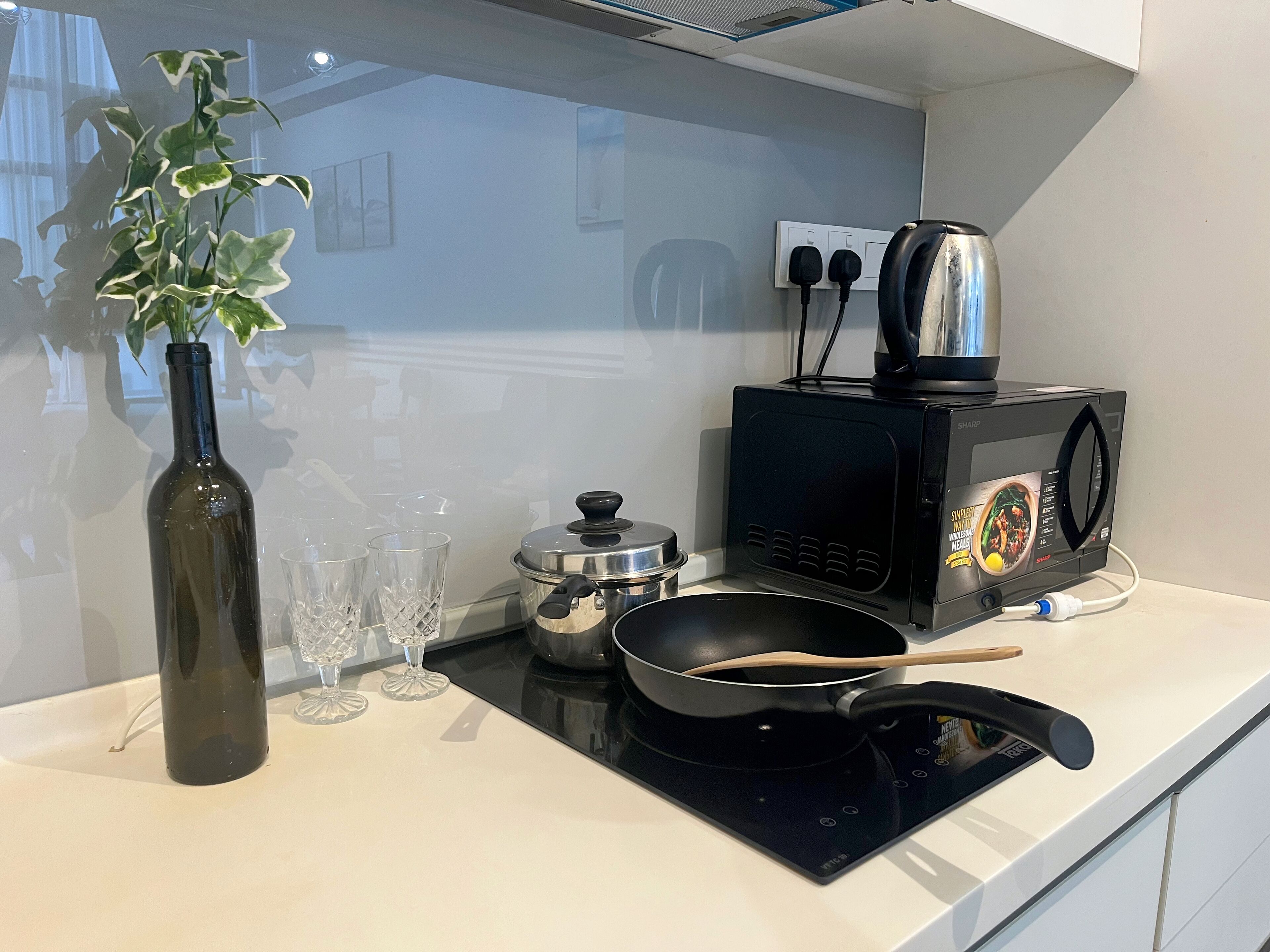 A kitchen counter with a microwave, a pan, a bottle, and glasses.