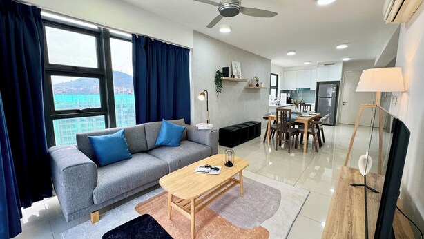 Ein modernes Wohnzimmer mit grauem Sofa, einem Holztisch und Blick auf eine Stadtlandschaft durch große Fenster.