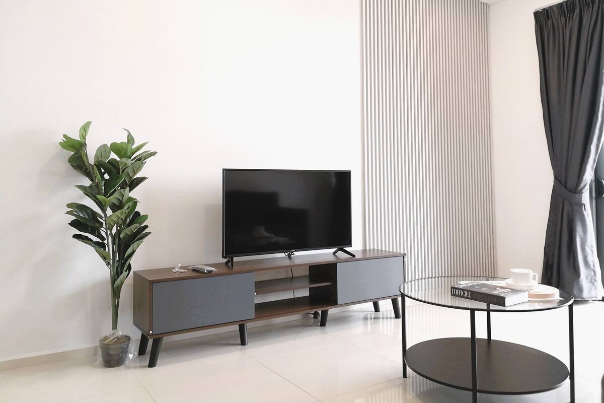 A modern living room with a flat-screen TV on a wooden TV stand, a potted plant, and a small round table with a book and a cup.