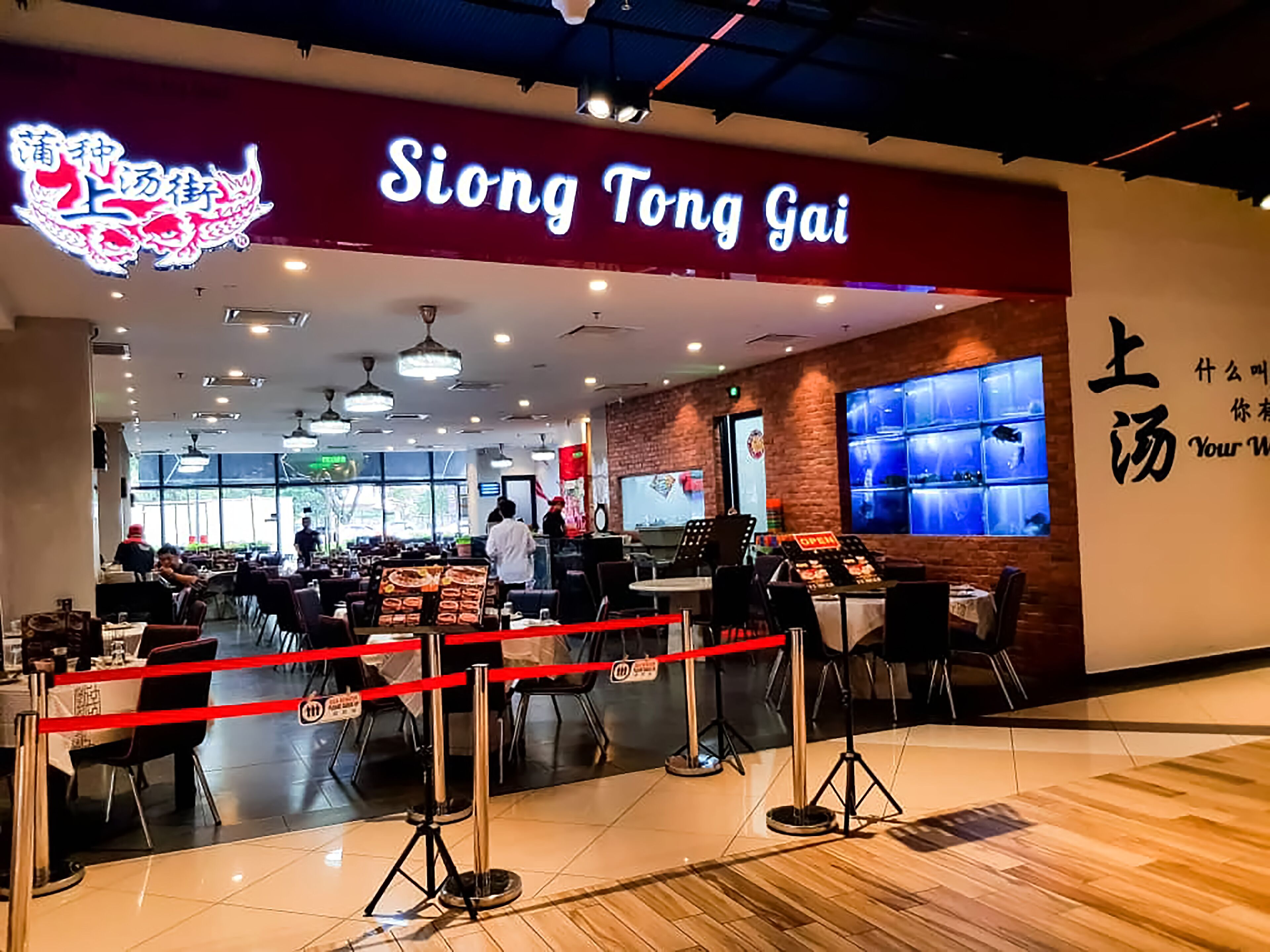 A restaurant interior with a red and white sign, tables, chairs, and a counter.
