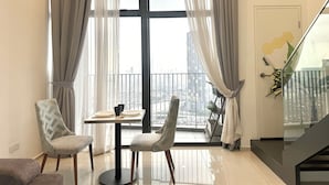 Ein modernes Wohnzimmer mit Essbereich, großen Fenstern mit transparenten Vorhängen, Blick auf die Stadtlandschaft und einer Treppe mit Glastrennwand.