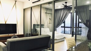 Ein modernes Hotelzimmer mit einer Couch, einem Fernseher, einem Bett, einer Glastrennwand und Blick auf die Stadt.