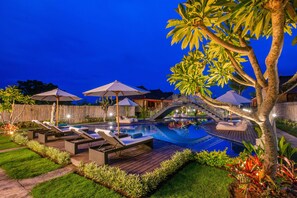 Un área junto a la piscina con sillones, sombrillas y una terraza de madera.