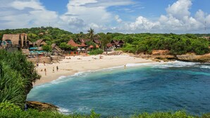 Ein Strand mit klarem türkisblauem Wasser, einem Sandufer und strohgedeckten Hütten.