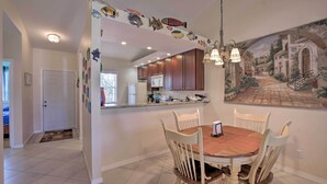 Uma sala de jantar com uma mesa redonda e cadeiras, uma cozinha com armários de madeira e um mural na parede.