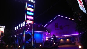 Un motel avec une enseigne au néon et plusieurs panneaux indiquant les services proposés.