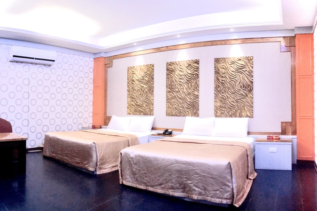 A hotel room with two beds, a desk, a chair, and a nightstand.