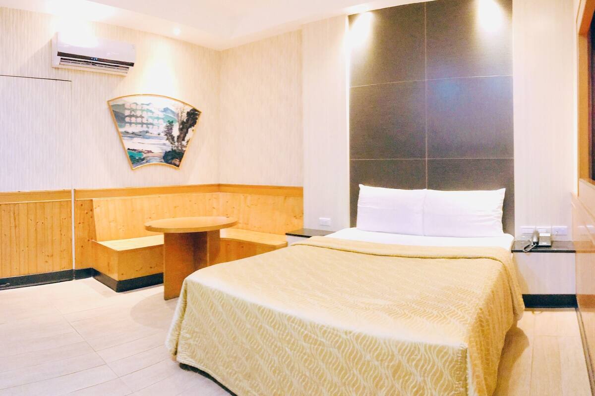 A hotel room with a bed, a round table, a small sink, and a wall-mounted air conditioner.