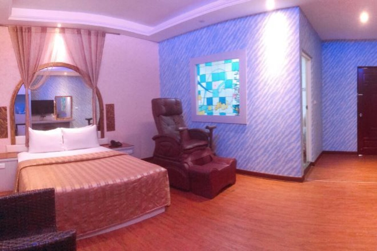A hotel room with a bed, a chair, a desk, and a large window with a view.
