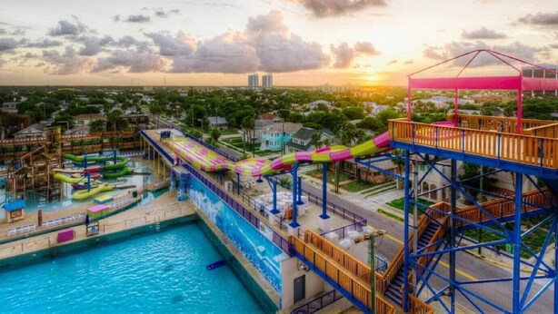 A water park with a pool, slides, and a sunset in the background.