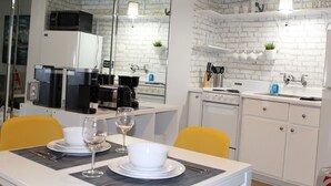 A modern kitchen with white brick walls, a dining area with yellow chairs, and a large mirror reflecting the kitchen.