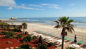 A beach view with a wooden deck, lounge chairs, and a palm tree.