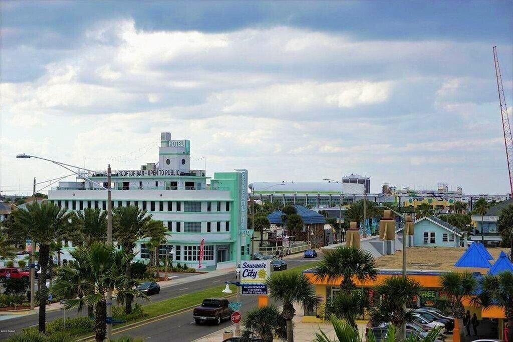 Un hôtel doté d’un bar sur le toit, d’une enseigne indiquant « Souvenir City », et offrant une vue sur les environs, notamment les palmiers et les autres bâtiments.
