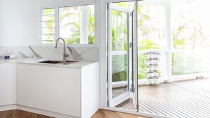 A modern kitchen with a sink, cabinets, and a view of a tropical garden through large windows. - POOL - OCEAN VIEWS - PET FRIENDLY (SUNSHINE BEACH)