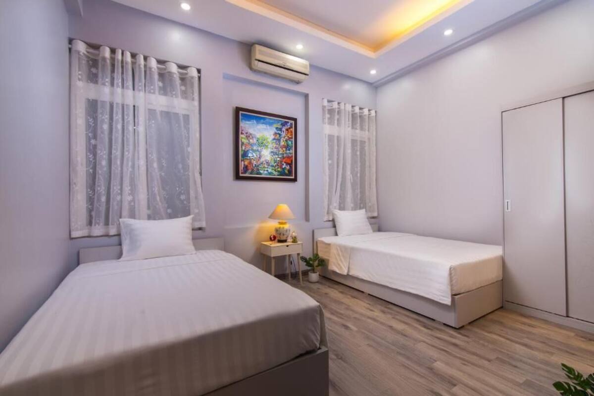 A bedroom with two beds, a nightstand with a lamp, a painting on the wall, and an air conditioning unit.