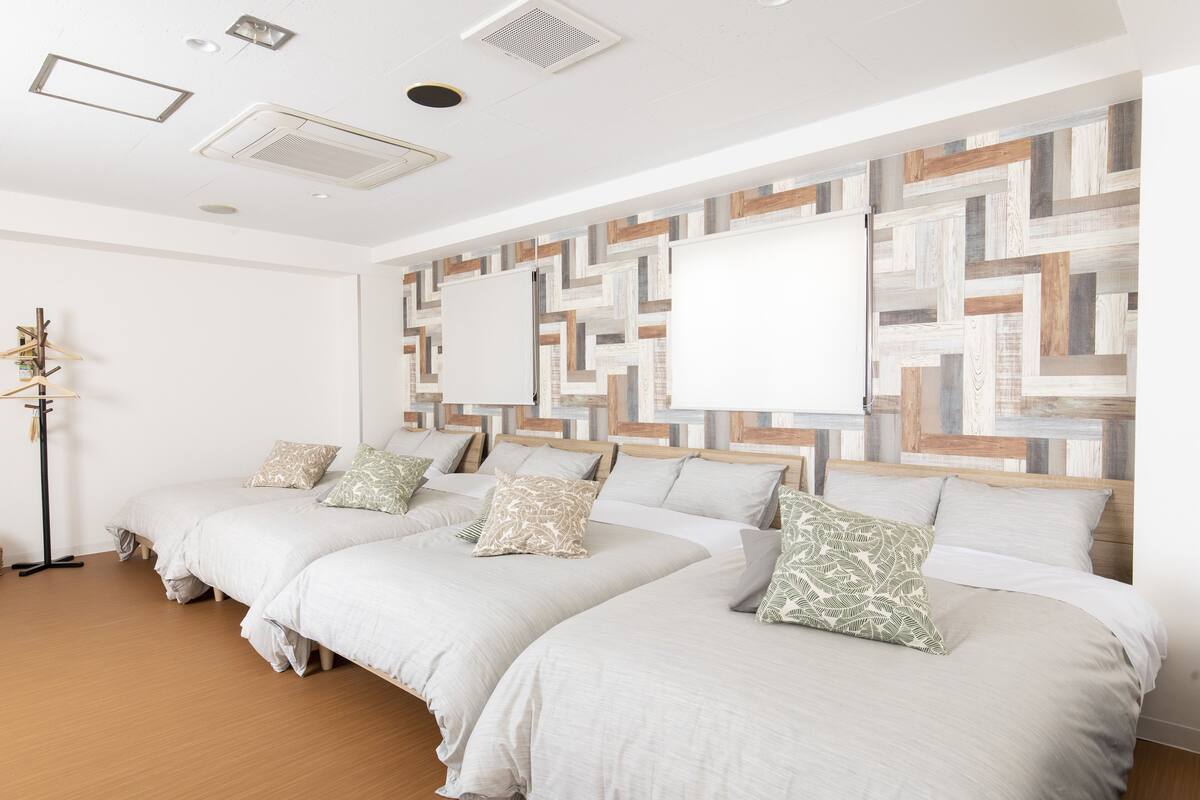 A hotel room with three beds, a wooden floor, and a wall with a geometric pattern.