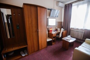 Quarto de hotel com guarda-roupa, escrivaninha, cadeira, mesinha e televisão.