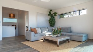 A modern living room with a grey sectional sofa, a woven coffee table, and a large plant. - Onetangi Oasis - fabulous home with pool & great views! (Onetangi)