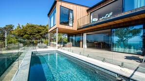 A modern house with a swimming pool, large windows, and a wooden deck. - Onetangi Oasis - fabulous home with pool & great views! (Onetangi)