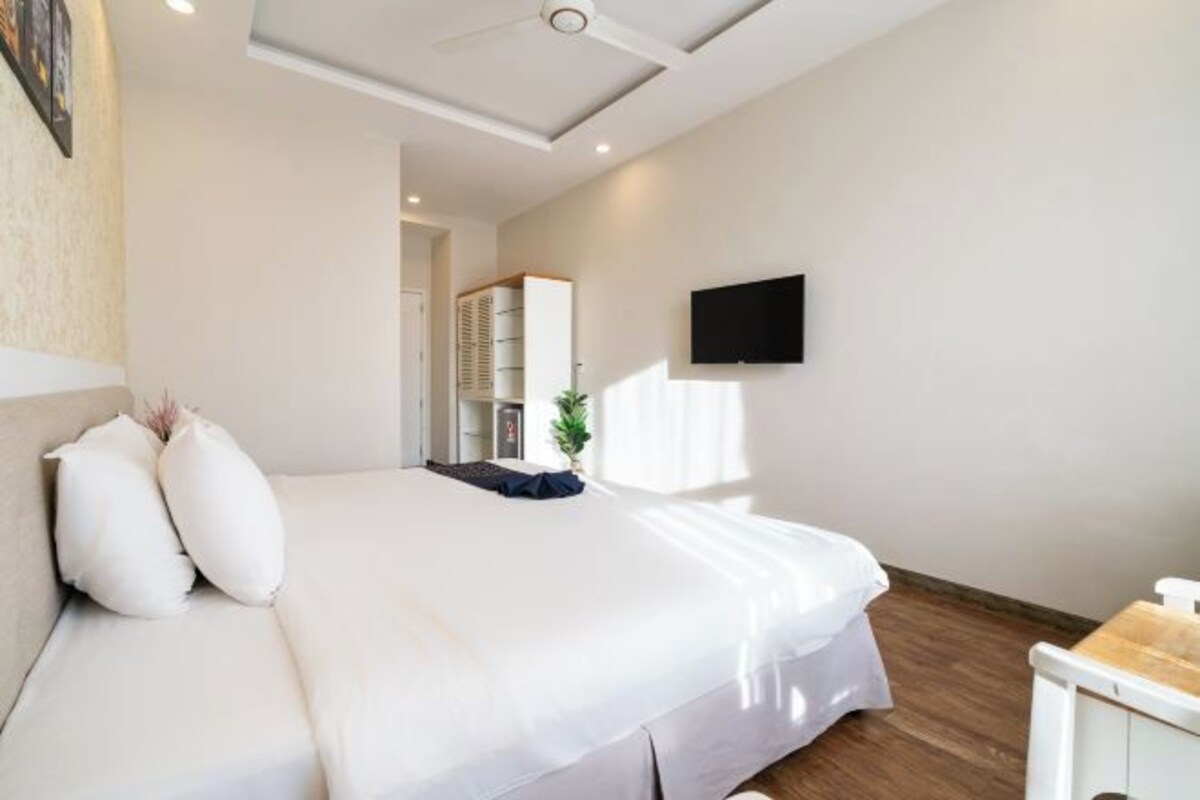 Una habitación de hotel moderna con una cama grande, un televisor de pantalla plana montado en la pared y suelo de madera.