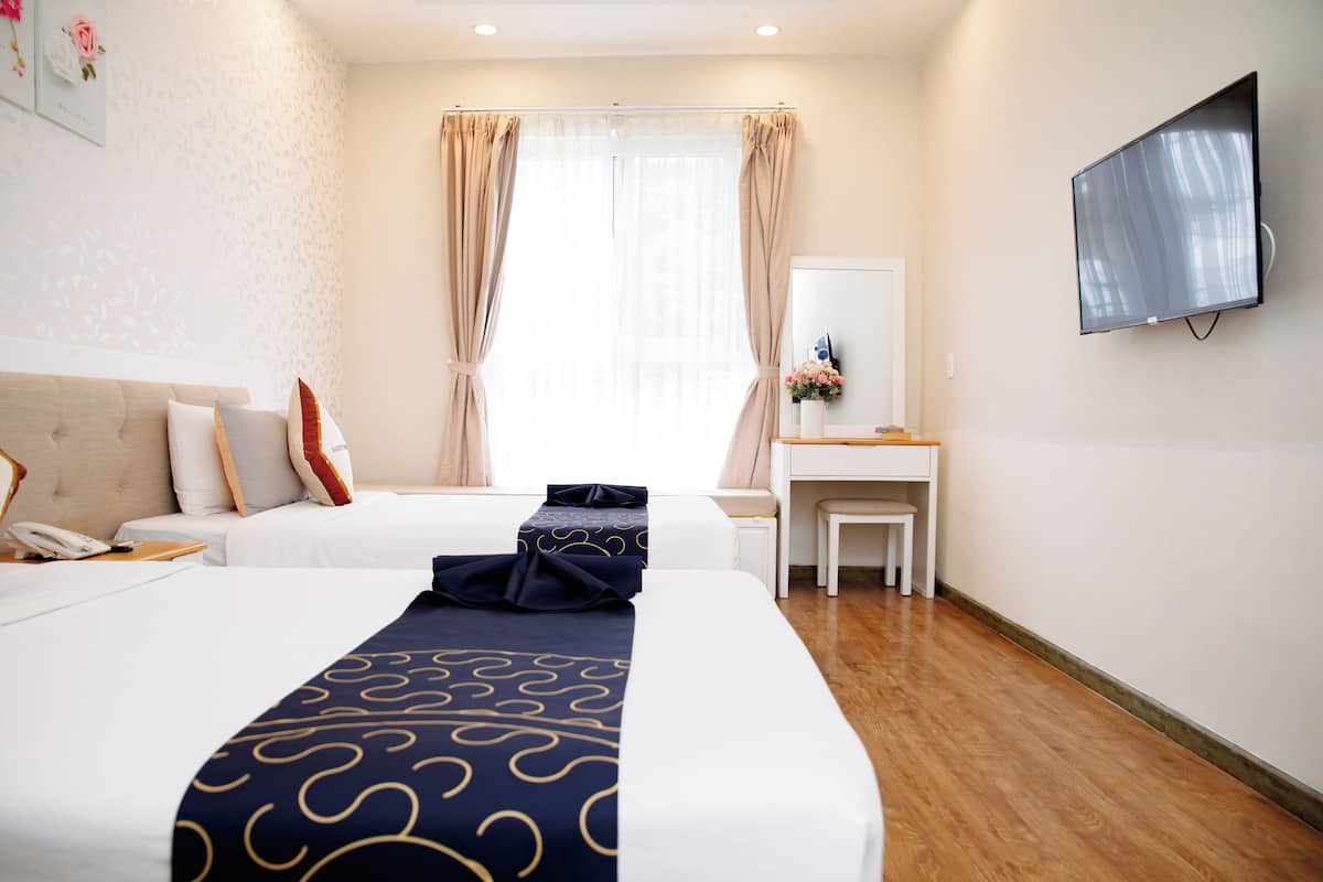 Ein Hotelzimmer mit zwei Betten, einem Schreibtisch, einem Stuhl, einem Fernseher und einem Fenster mit Vorhängen.