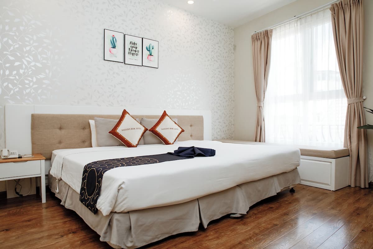 Ein ordentlich eingerichtetes Schlafzimmer mit einem großen Bett, einem Nachttisch mit Telefon und einem Fenster mit Vorhängen.