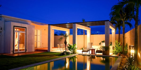 A modern outdoor pool area with a glass-enclosed patio, seating, and a well-maintained lawn. - Private House YOSHINO (Miyakojima)
