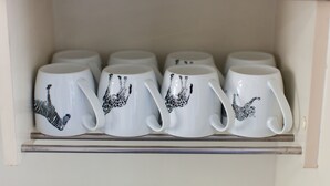 En hylla med sex vita muggar dekorerade med zebrastriemönster.
