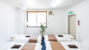 Ett hotellrum med två sängar, ett fönster, en växt och en dörr med en skylt som visar var nödutgången finns.