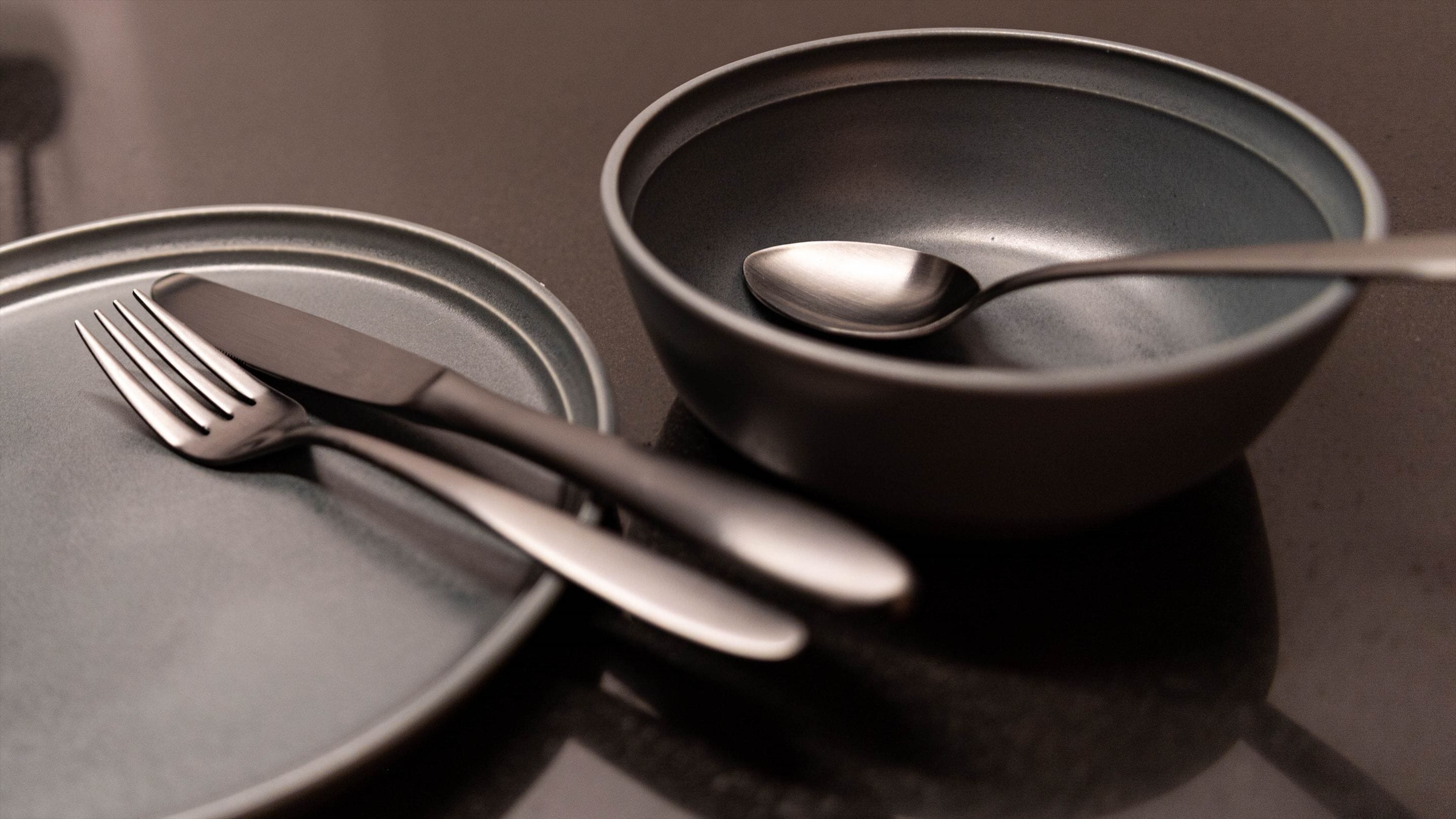 A dark-colored table with a fork, knife, and spoon placed on a plate.