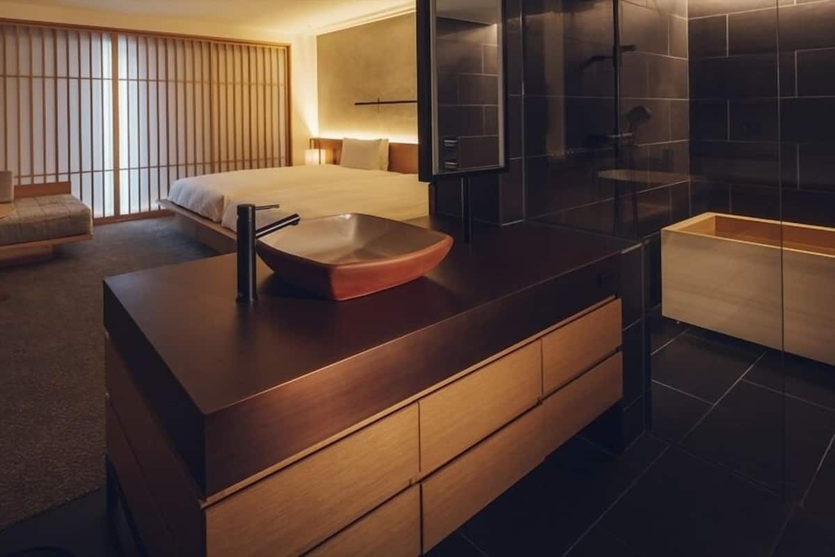 A modern hotel room with a large bed, a wooden vanity with a sink, a small table, and a seating area with a sofa and chairs.