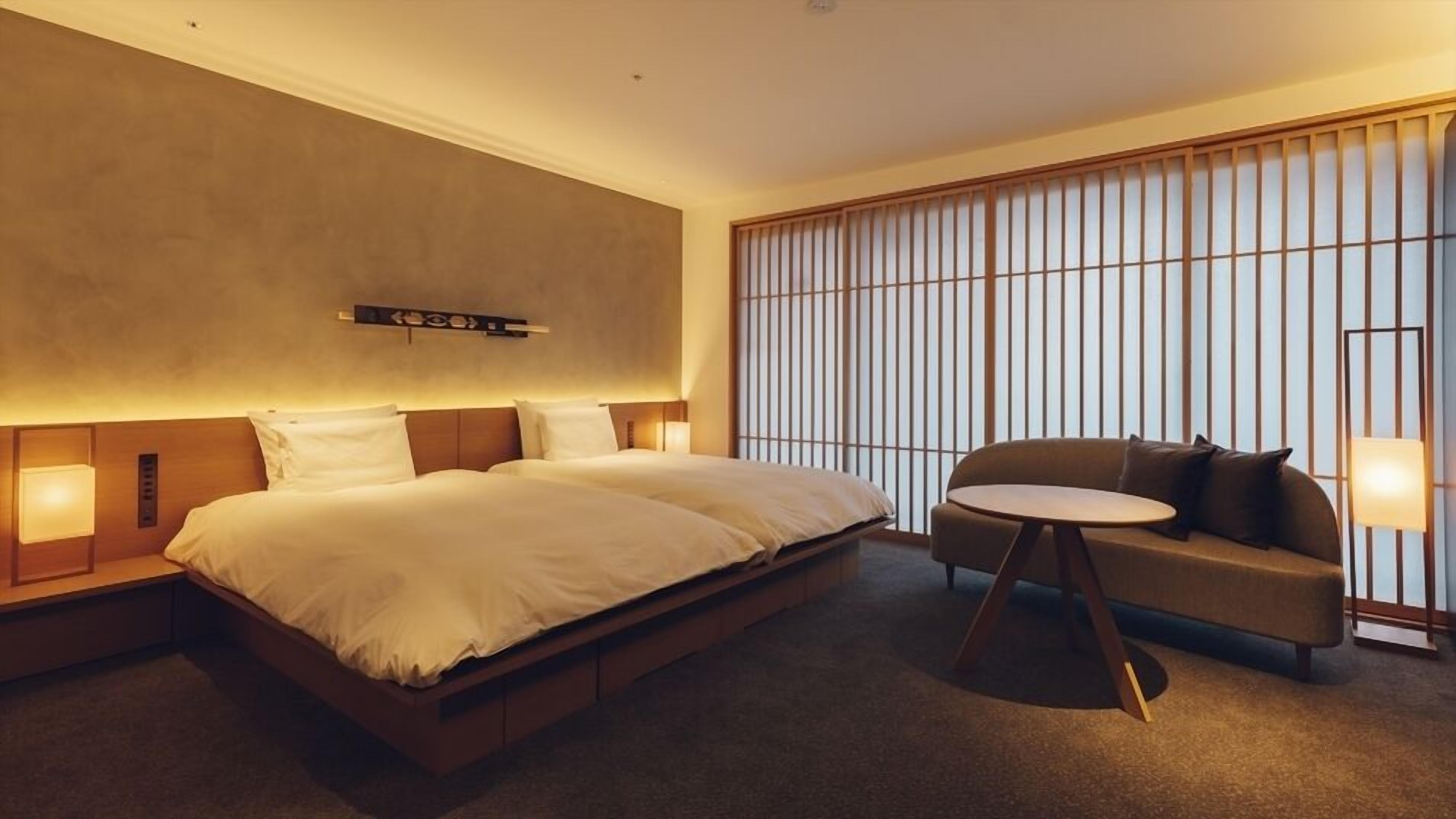 A hotel room with a large bed, a sofa, a small table, and a sliding shoji screen.