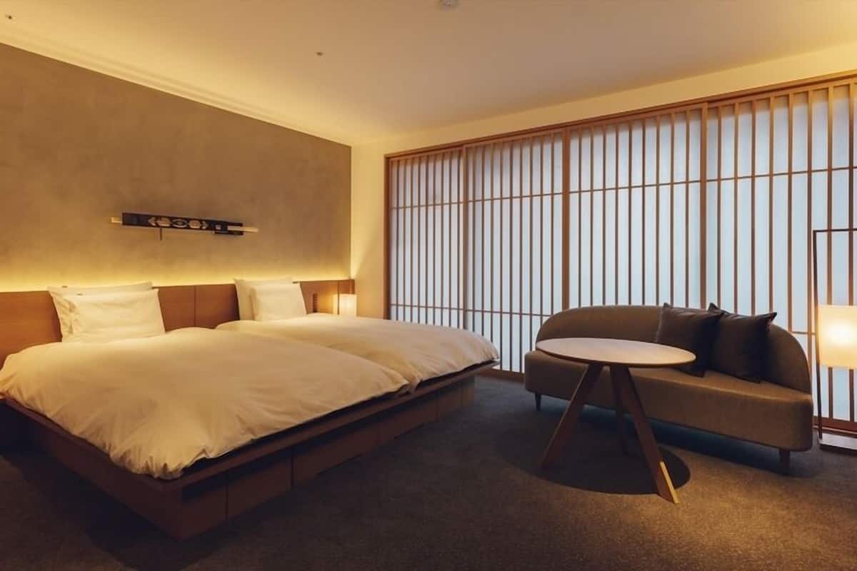 A hotel room with a large bed, a sofa, a small table, and a sliding shoji screen.