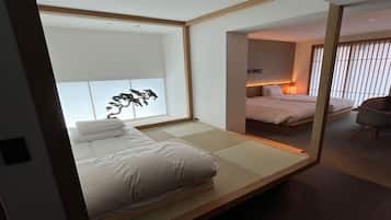 Una habitación japonesa minimalista con suelo de tatami, una cama baja, un futón, un panel shoji y una escultura tradicional de árbol japonés.