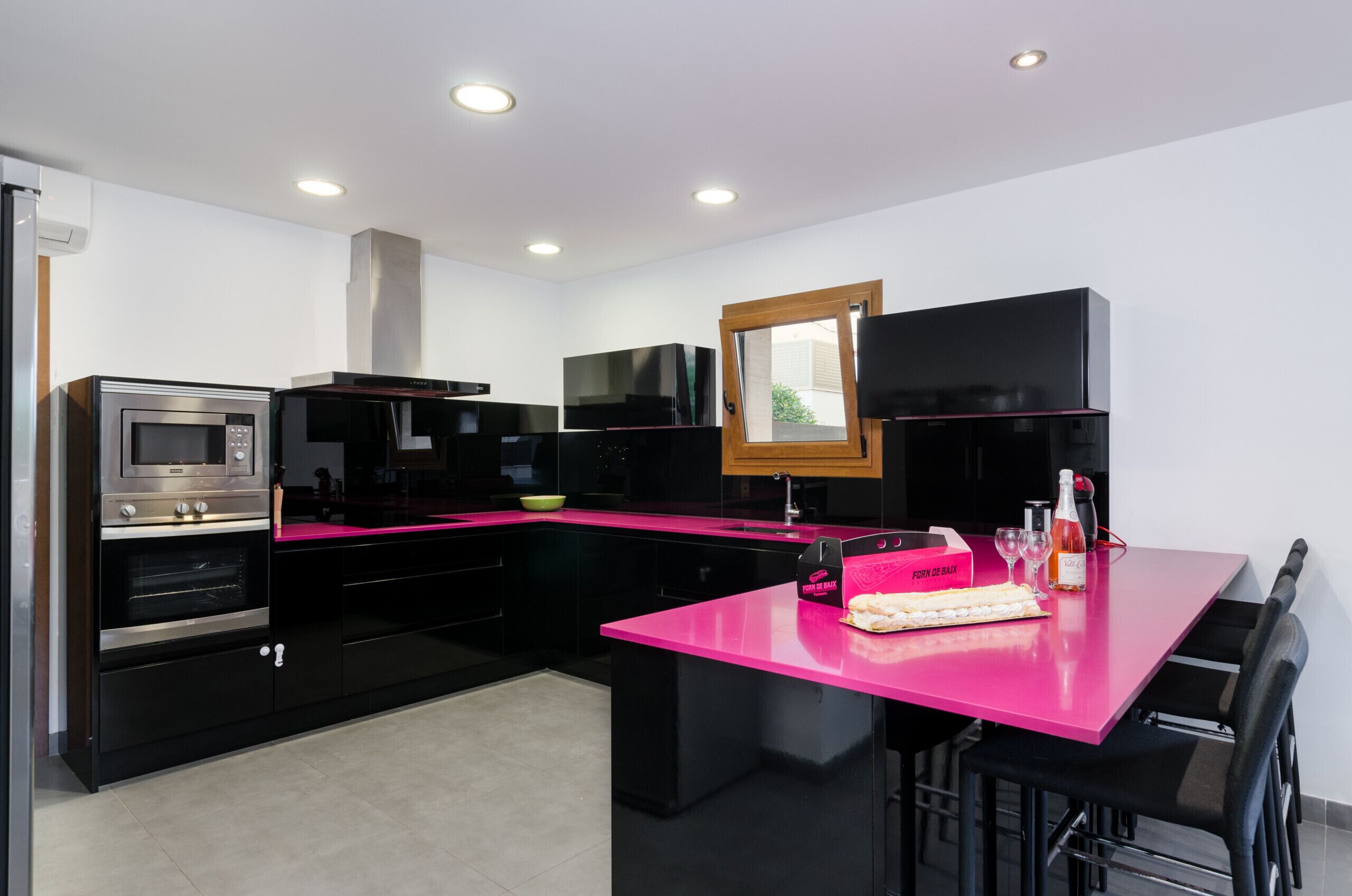 Una cocina moderna con gabinetes negros, encimera rosa y electrodomésticos integrados, incluyendo un microondas y un horno.