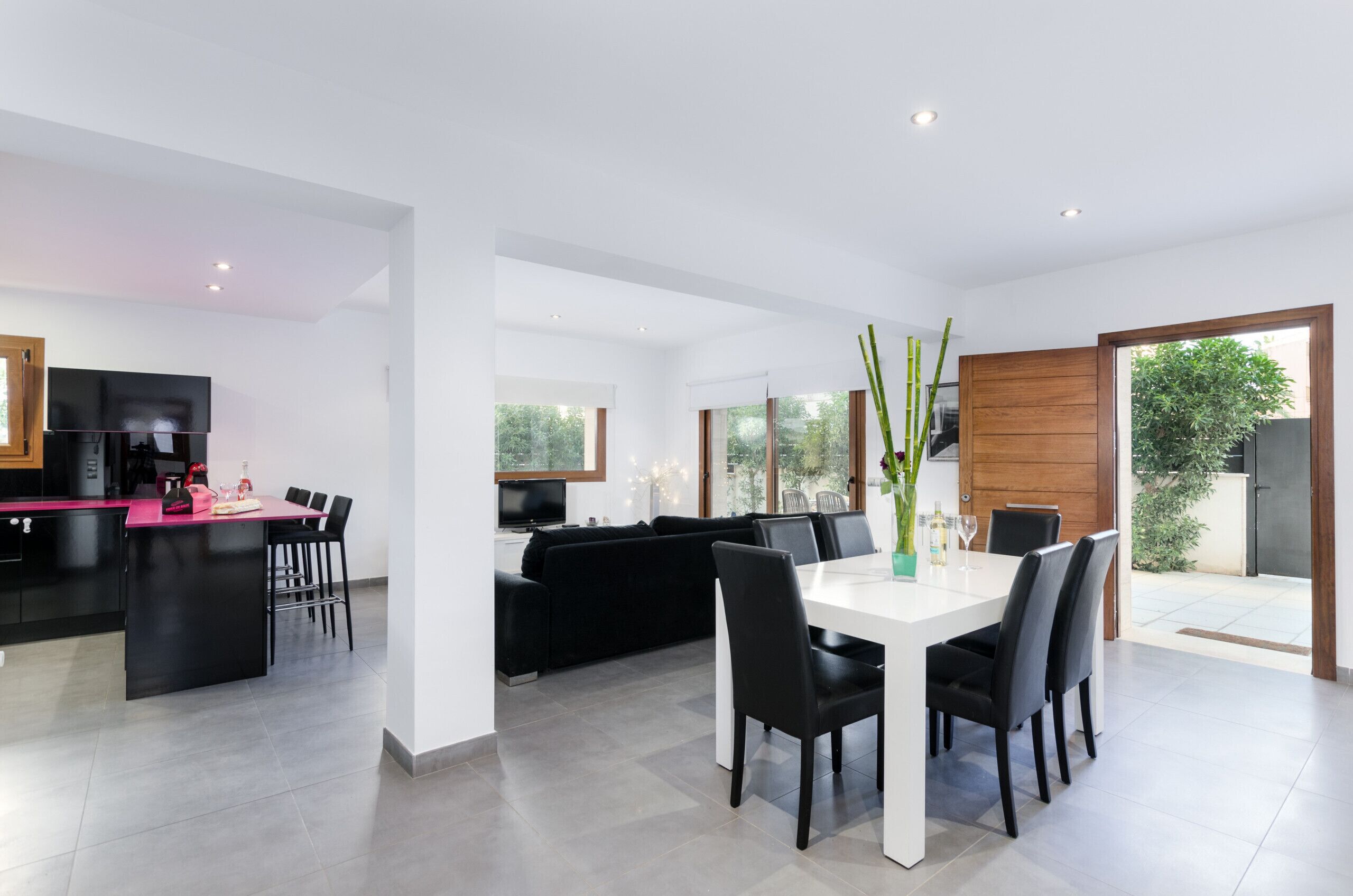 A modern kitchen with a black island, a dining area with a white table and black chairs, and a black sofa in the living area.