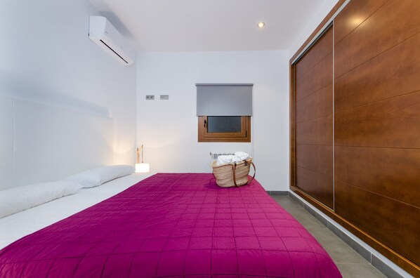 A bedroom with a bed, a window, a wooden wardrobe, and an air conditioning unit. - YourHouse Cardinal (Can Picafort)