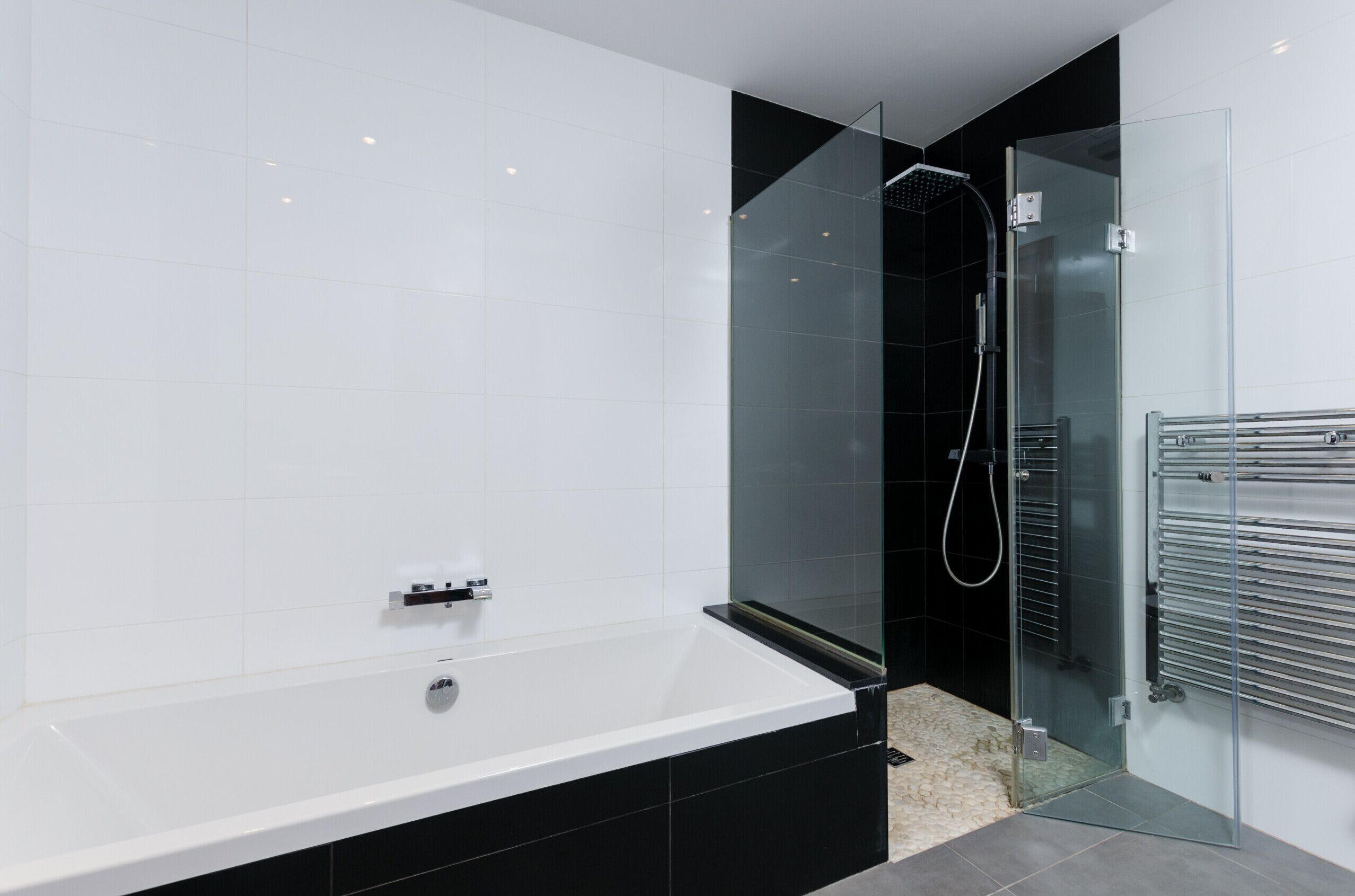 A modern bathroom with a glass-enclosed shower, a white bathtub, and a black tiled wall.