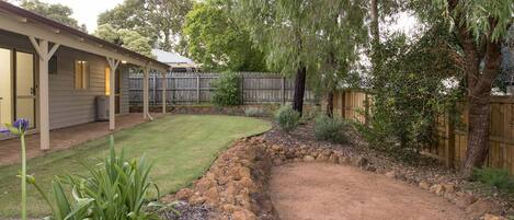 Un patio trasero con césped cuidado, un muro de contención de piedra y una variedad de plantas.