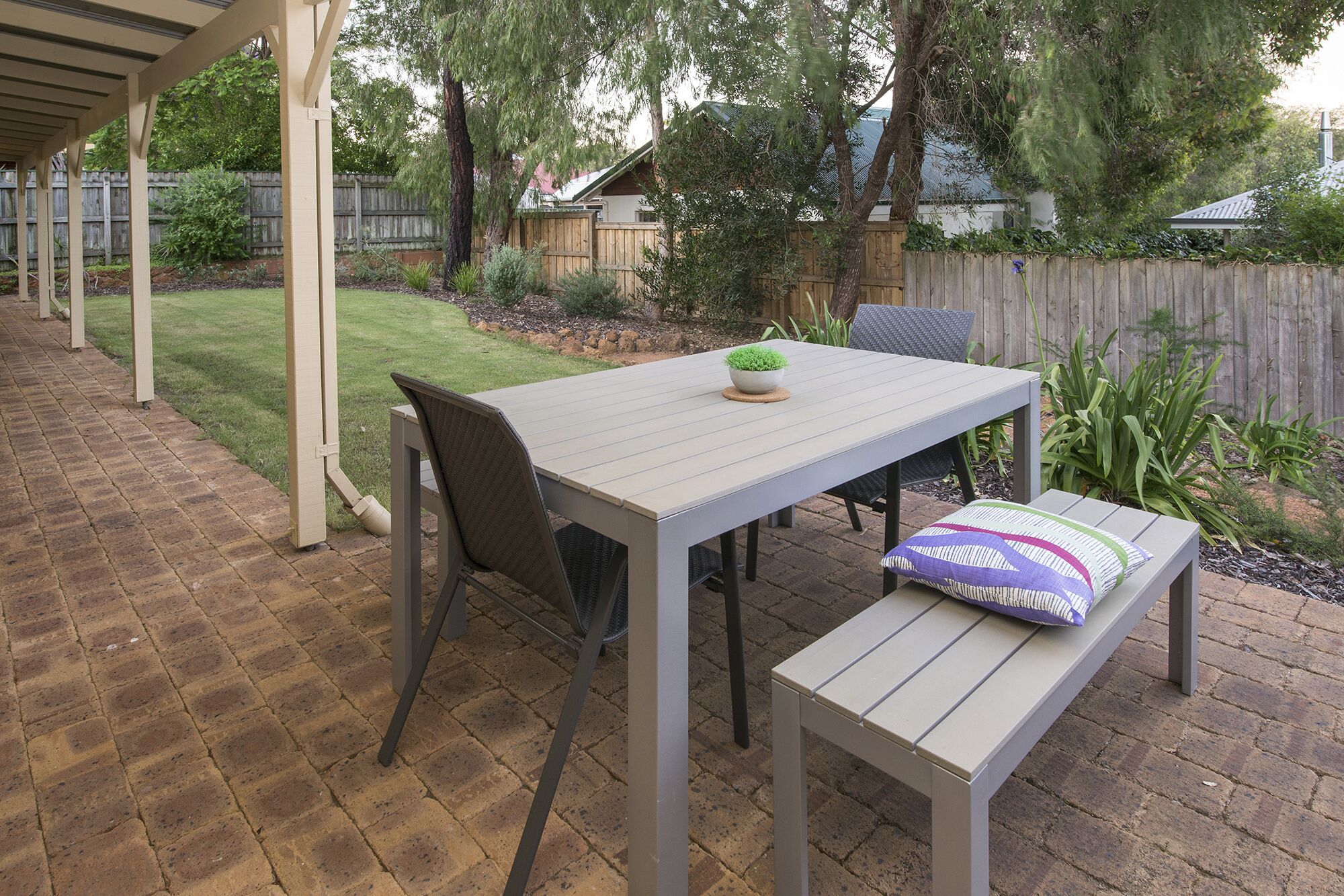 An outdoor patio with a table and chairs, a bench, and a small potted plant.