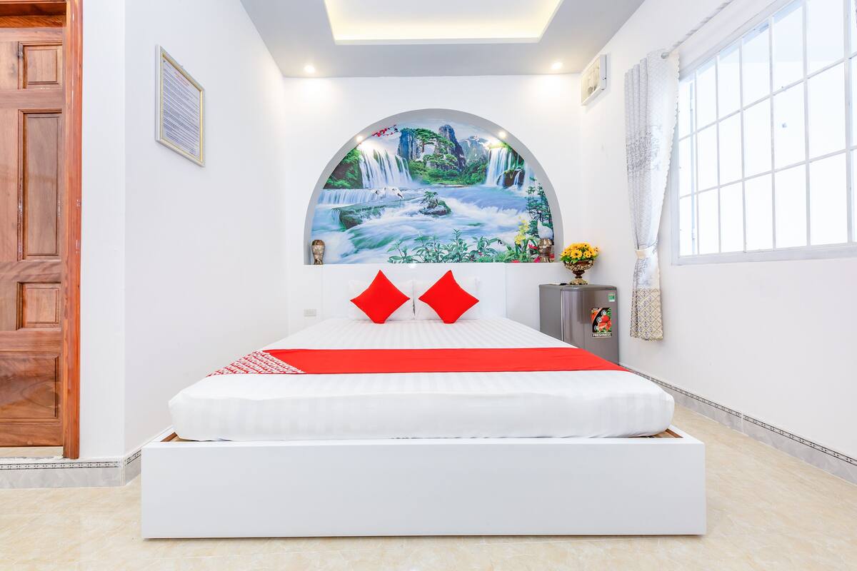 A modern bedroom with a white bed, red pillows, a mural of a waterfall, and a window with curtains.