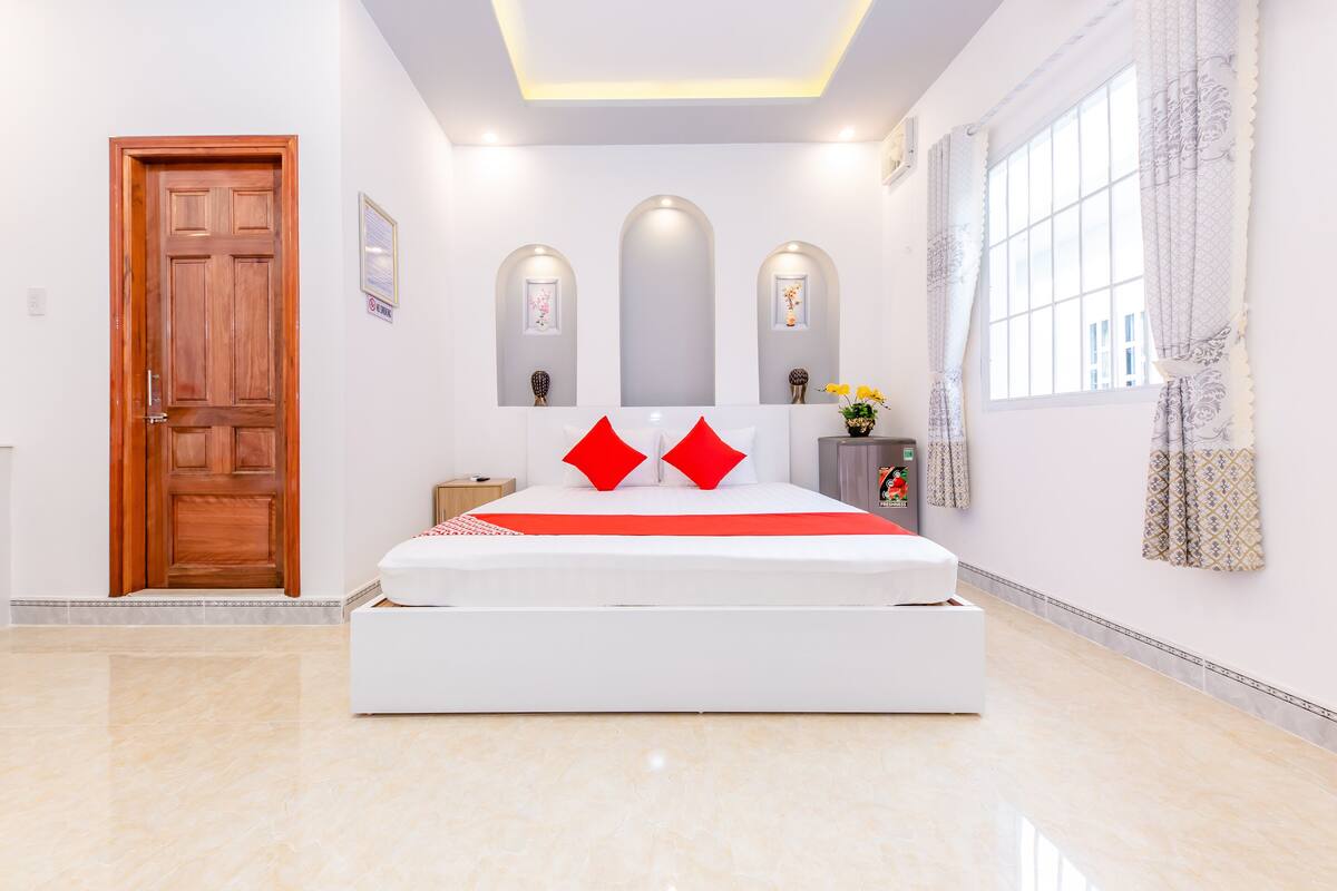 A bedroom with a large bed, a wooden door, and a window with curtains.