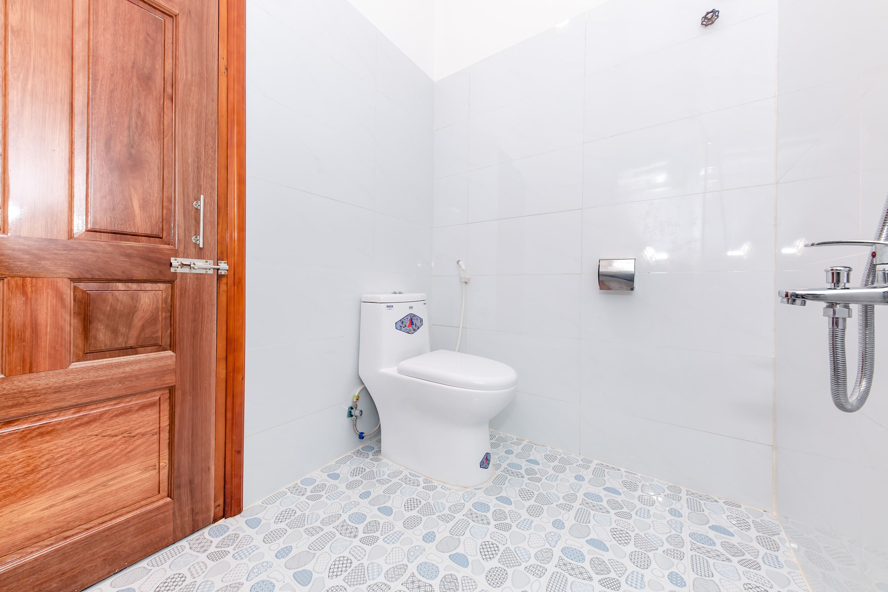 A bathroom with a wooden door, white tiles, a toilet, and a shower area.