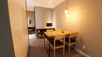 A compact room with a wooden dining table and chairs, a small desk with a computer, and a hanging light fixture.