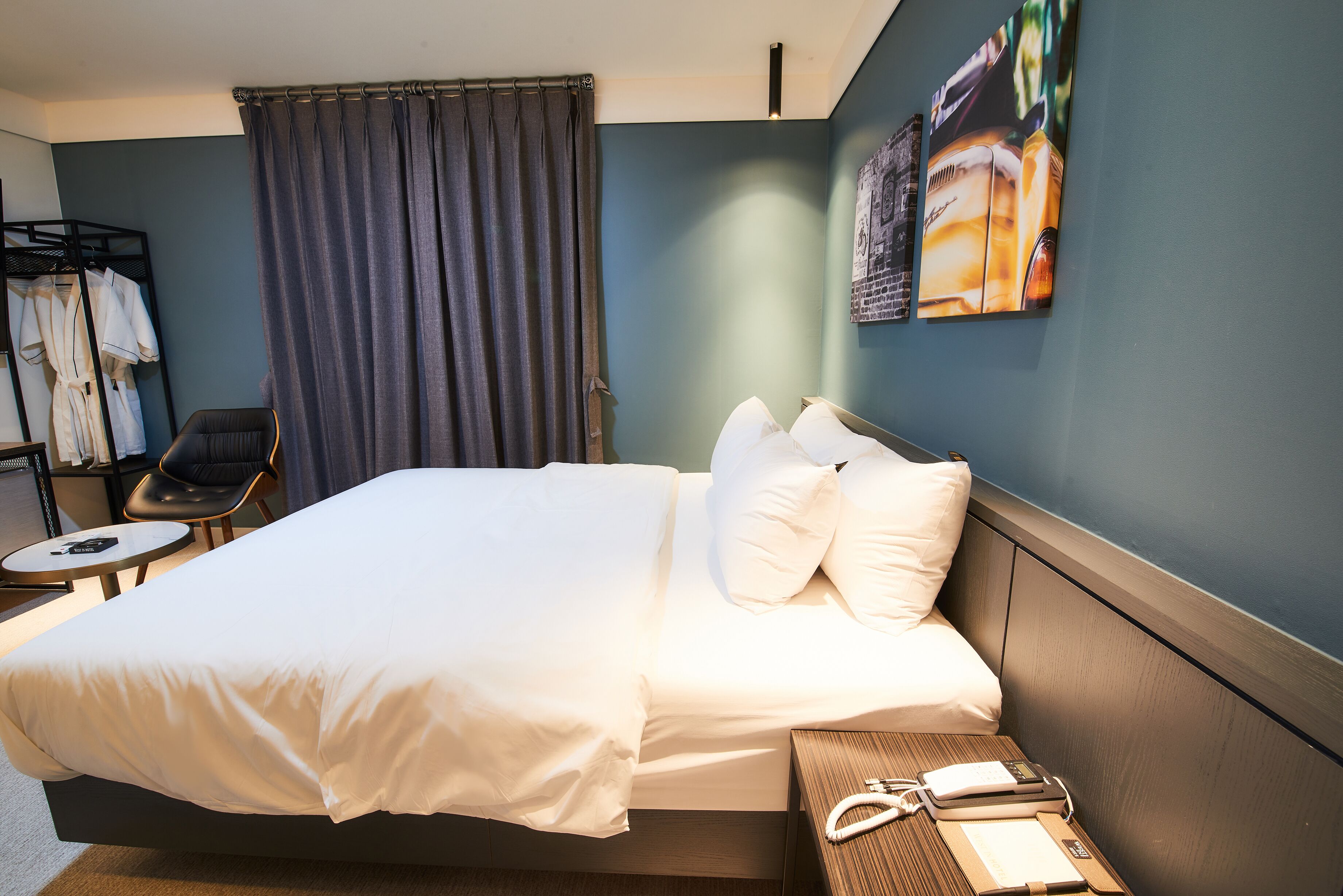 A hotel room with a large bed, a chair, a small table, and a wall-mounted artwork.
