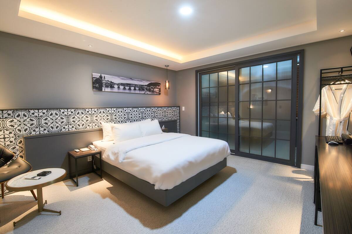 Una habitación de hotel moderna con una cama grande, una mesita de noche, una silla, un escritorio y un armario.