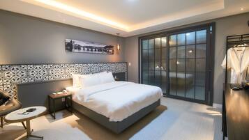 A modern hotel room with a large bed, a nightstand, a chair, a desk, and a wardrobe.
