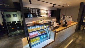 Una cafetería moderna con una vitrina refrigerada de bebidas, un panel de menú y una barra con equipos para preparar café.