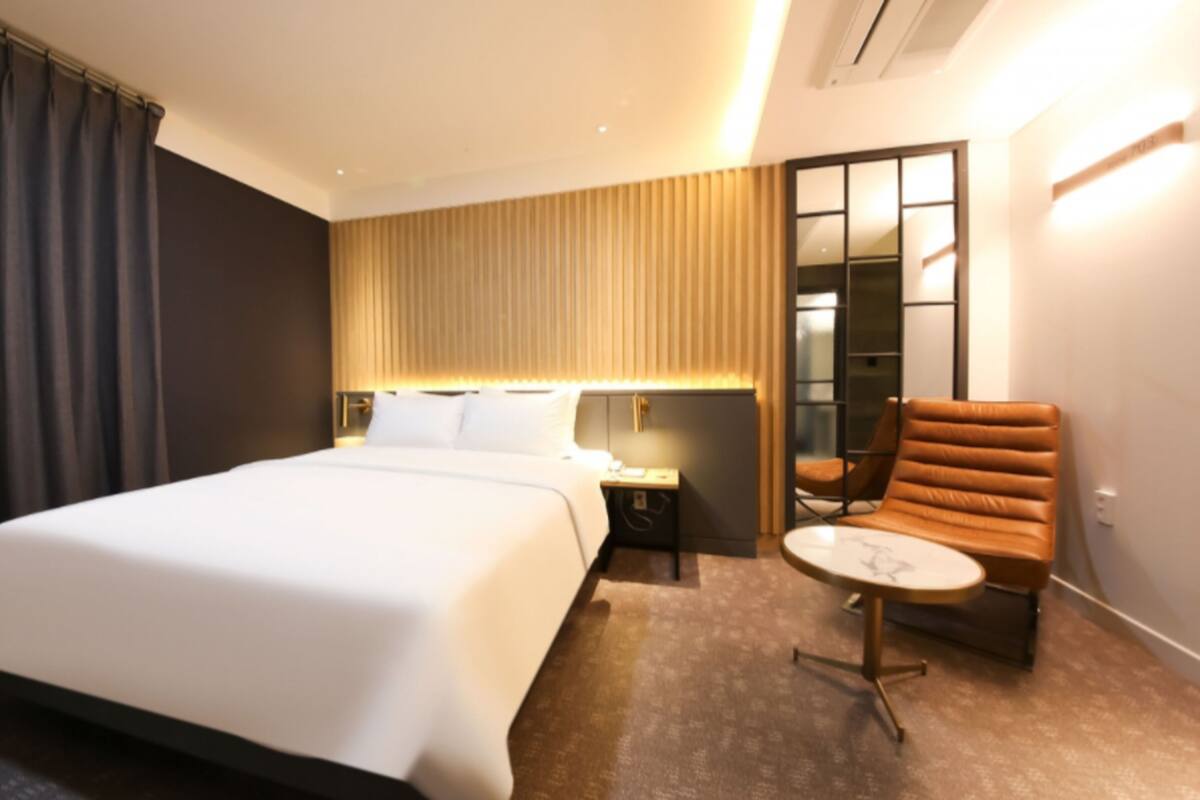 Una habitación de hotel moderna con una cama grande, una mesita redonda pequeña, una silla y una mesita de noche.