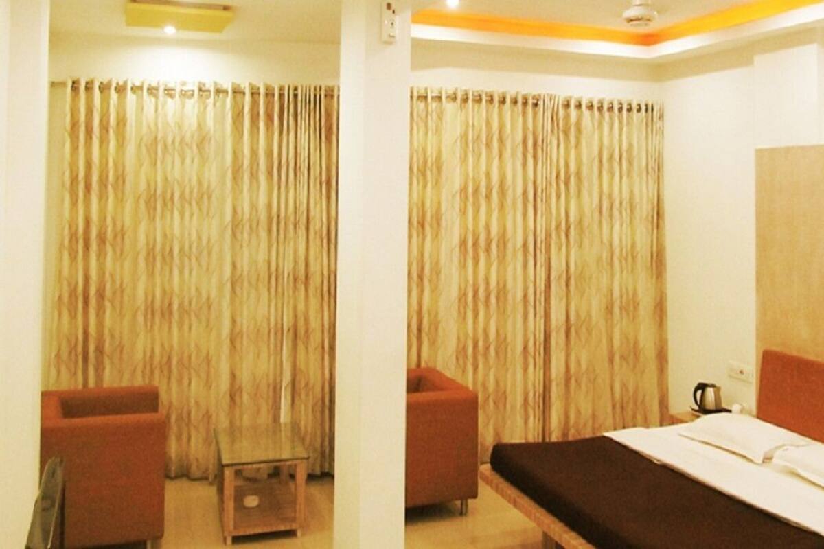 A hotel room with a bed, a small table, two chairs, and a large window with curtains.